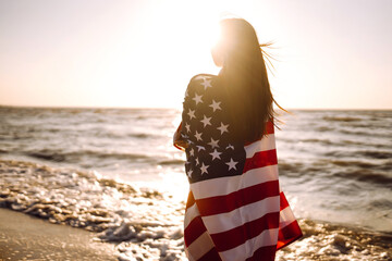 Girl with american flag on the beach at sunset. 4th of July. Independence Day. Patriotic holiday.