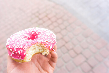 Bitten pink donut in hand. doughnut with a pink chocolate frosting. Sweet dessert festive. Breakfast and bachelorette party concept. Unhealthy food with high calorie content. Snack and junk food habit