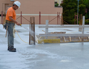 Construction worker watering fresh concrete slab using a hose