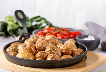 Roasted small whole potatoes in a cast iron skillet on concrete background. Vegetarian or vegan food concept.