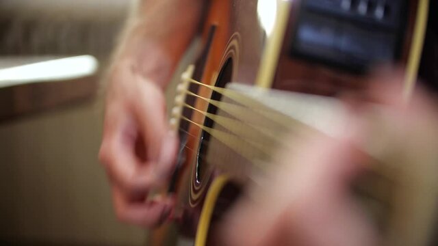 Detail of a guy playing acoustic guitar with a plectrum