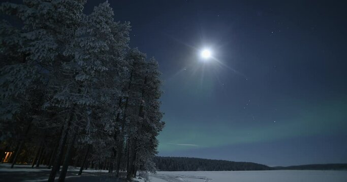 Northern lights time lapse of aurora borealis and moon at night, with stars. Timelapse over remote landscape of frozen lake and forest in Lapland, Finland