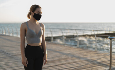 Fototapeta premium beautiful girl in a medical respirator by the ocean. women's sport cloths. Place for text.