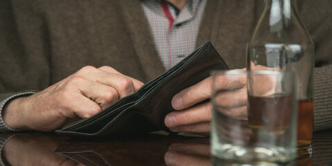 old man holds black wallet reflecting on brown wooden table with cognac bottle closeup