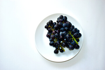 Black and delicious grapes on a white plate