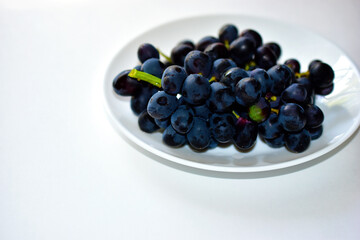 Black and delicious grapes on a white plate