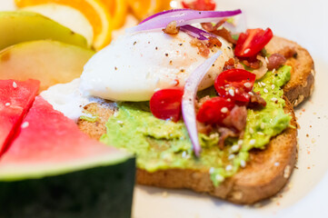 Breakfast for a healthy lifestyle. Avocado toast, poached egg and sliced fruit.