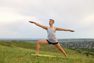 Fototapeta na wymiar Mature man doing yoga exercise Valence on green grass in nature.