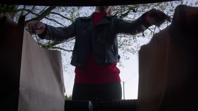 Caucasian Handsome Female Loads Shopping Bags From Eco Paper Bags Into Car Trunk. Loading Paper Bags With Groceries From The Supermarket Into Boot Of Car. View From The Trunk.