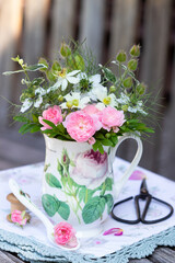 Blumenstrauss mit pink Rosen und Nigella damascena in Tasse mit Rosenmotiv