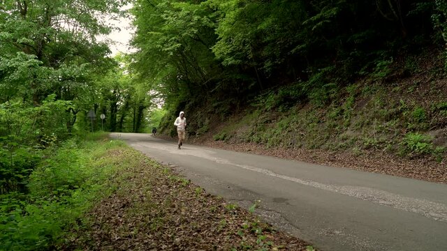 Image of a man jogging alone at calm road surrounded by forest, Croatia.