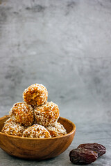 Homemade vegan sweets without sugar from dates, carrots, coconut flakes in a wooden bowl close-up on a dark background, vertical background, healthy eating concept