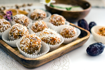  Healthy raw energy balls.Candies vegan balls of dates, coconut pulp, carrots on a wooden tray in paper molds. Top view, concept of useful homemade sugarless candies, coconut energy balls. 