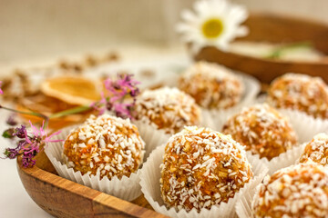 Healthy raw energy balls.Candies vegan balls of dates, coconut pulp, carrots on a wooden tray in paper molds. Top view, concept of useful homemade sugarless candies, coconut energy balls. 