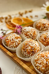  Healthy raw energy balls.Candies vegan balls of dates, coconut pulp, carrots on a wooden tray in paper molds. Top view, concept of useful homemade sugarless candies, coconut energy balls. 