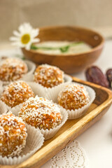  Healthy raw energy balls.Candies vegan balls of dates, coconut pulp, carrots on a wooden tray in paper molds. Top view, concept of useful homemade sugarless candies, coconut energy balls. 