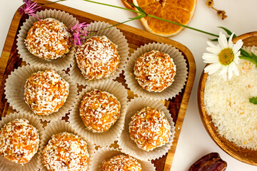 Healthy raw energy balls.Candies vegan balls of dates, coconut pulp, carrots on a wooden tray in paper molds. Top view, concept of useful homemade sugarless candies, coconut energy balls. 