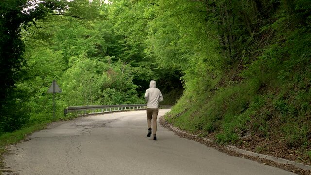 Image of a man jogging alone at calm road surrounded by forest, Croatia.