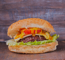 Cheese burger with relish, shot close up on a wooden surface with a wooden backdrop.