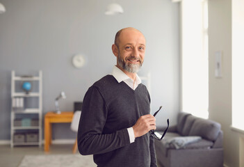 Portrait of a happy senior man smiling while standing in the living room. Confident experienced professional. - Powered by Adobe