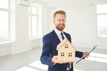Real estate agent holding a model of the house smiling in white real estate room apartment home.