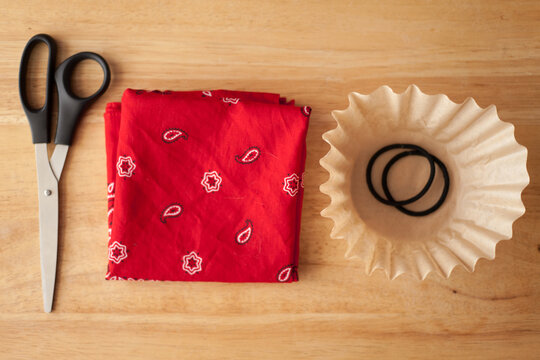 Materials For CDC Recommended Cloth Face Covering, An Easy DIY Face Mask. Flat Lay Of A Bandanna, Scissors, Coffee Filter, And Hair Ties Arranged In A Neat Line.