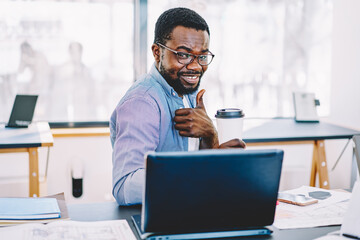 Portrait of cheerful african american male freelancer holding coffee cup showing ok sign enjoy break,successful dark skinned employee at desktop with laptop computer gesture thumb 