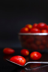 Fresh cherry tomatoes on a silver spoon placed on the table with water drops and a blur tomato basket background. Food photo concept in selective focus.