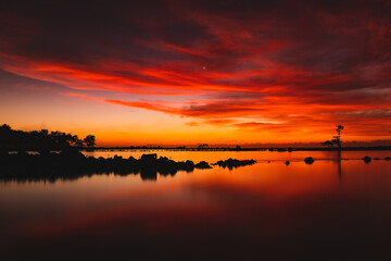 Obraz na płótnie Canvas orange sunrise between clouds, water and trees