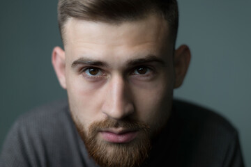 Fototapeta premium Portrait of a young bearded guy of twenty-five years old, looking at the camera, close-up. Studio photo on a gray background.