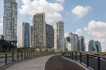 Naklejka premium empty footpath and cycling lane in La Mexicana park in Santa Fe, Mexico CIty with modern skyline of residential buildings behind