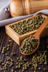 green peppercorns in wooden scoop on rustic background