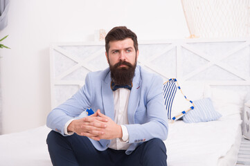 On wedding anniversary. Bearded man in wedding style sit on bed. Hipster wait in wedding suite. Formalwear and party wear. Fashion and style. Wedding shop