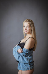 blonde beauty poses in black underwear and jeans against a dark background