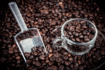 glass coffee cup, dish and spoon surrounded by black coffee beans