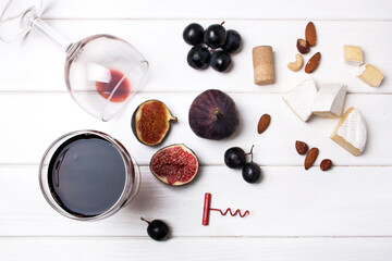 Flat lay two glasses of red wine, figs, and cheese on a white wooden background