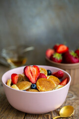 Pancake porridge, mini pancakes in a bowl with maple syrup. Dutch mini pancakes are called strawberry potato pancakes. Syrup is poured onto mini pancakes with strawberries and blueberries.
