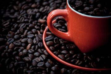 red coffee cup and dish filled with black coffee beans, with the same beans in the background