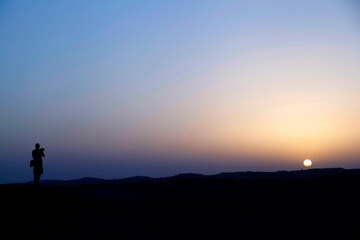 Fototapeta na wymiar silhouette of a man taking photo in Dubai desert at sunset
