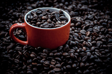 red coffee cup filled and surrounded by black coffee beans