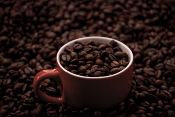 Fototapeta premium red coffee cup filled and surrounded by black coffee beans