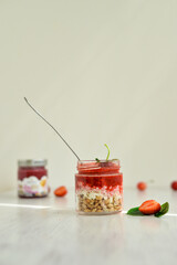 Strawberry dessert with granola and cottage cheese in glass jar on the white table 