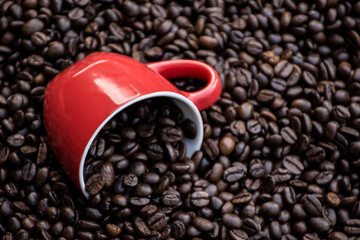 red coffee cup filled and surrounded by black coffee beans