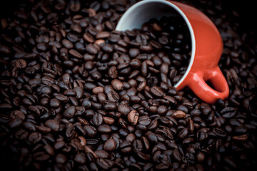 red coffee cup filled and surrounded by black coffee beans
