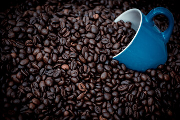 blue coffee cup filled with black coffee beans and surrounded by them