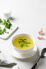 Chicken broth with onion, greens in white bowl isolated over white table. Vertical format.