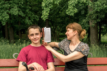 Family vacation in the park on a bench. Mom and son spend time outdoors reading an interesting book. Pleasant and useful - rest and enlightenment. Dialogue of generations..