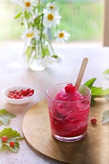 Summer dessert, fruit ice or frozen sorbet or granite from red currant puree and sugar syrup in a glass on a light concrete background. Frozen desserts.