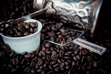 coffee pot, spoon and cup filled and surrounded by coffee beans