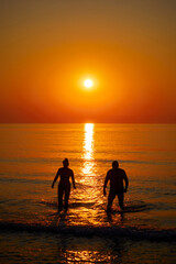 Fototapeta premium Silhouette of a couple swimming in the sea at sunrise
